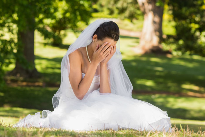 Bride in wedding dress sitting outdoors covering her face, upset about wedding date ownership dispute with cousin. Bride in wedding dress sitting outdoors covering her face, upset about wedding date ownership dispute with cousin.