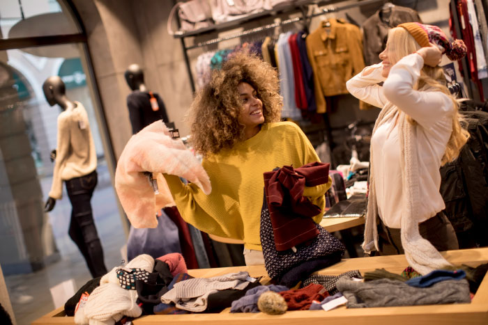 Two women shopping for clothes, sharing opinions and enjoying a lively conversation in a boutique setting.