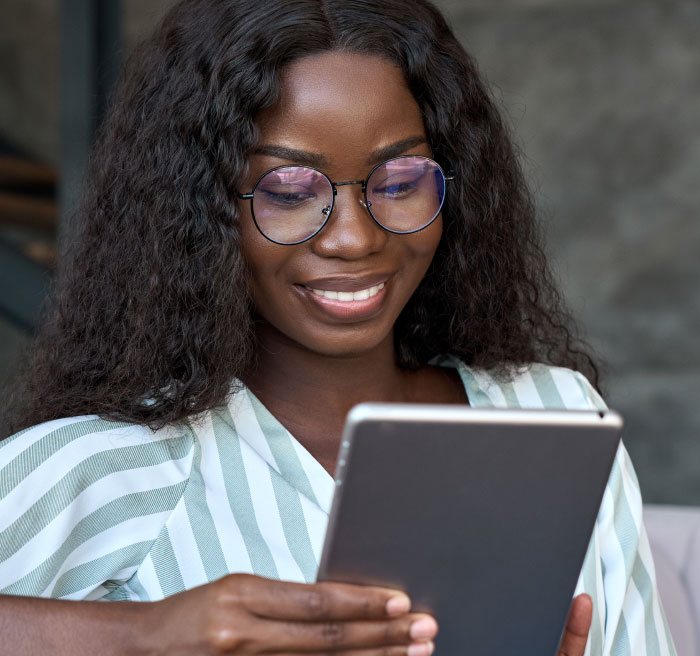 Young woman wearing glasses smiling while holding a tablet, reading opinions about boomer culture and trends.