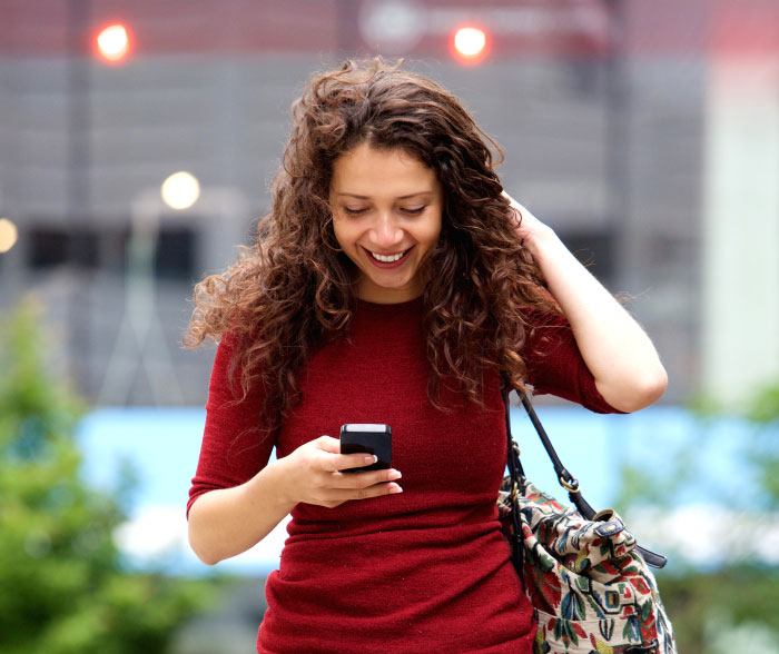 Young woman in a red dress smiling while using her phone outdoors, reflecting on boomer opinions and trends.