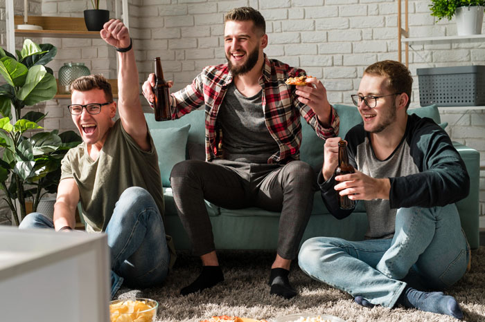 Three men cheering with beers and pizza in a living room, boyfriend ban friends relationship topic