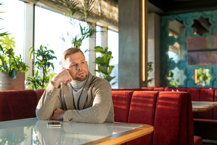 Man reflecting alone in a cafe, appearing thoughtful after a teenage bullying incident and relationship fallout.