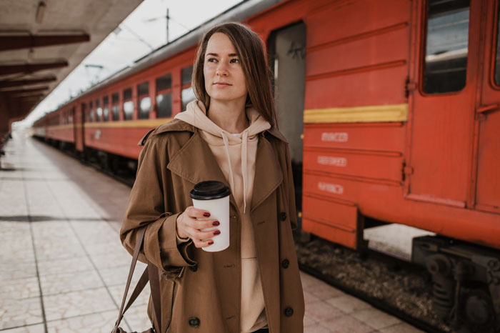 Woman holding coffee cup standing by a red train at the station, reflecting on bullying and relationship reversal.