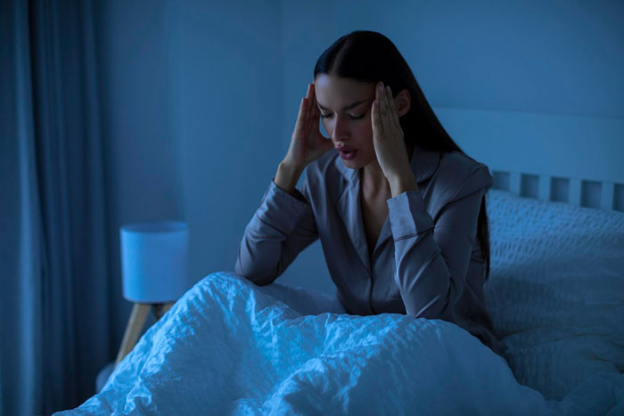 Woman sitting in bed holding her head, experiencing trauma triggered by boyfriend&rsquo;s family Christmas tradition.