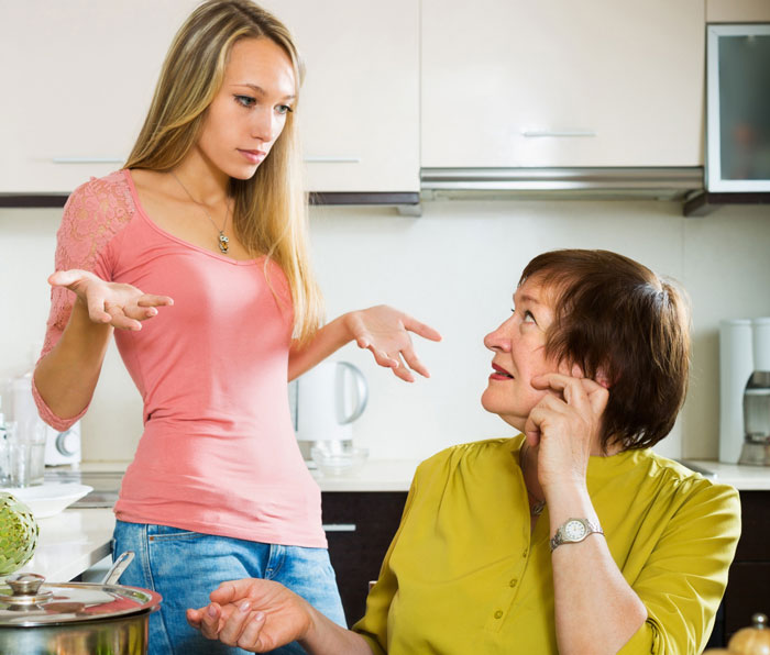 Young woman looking frustrated while talking to older woman in kitchen, feeling like a guest in her own home.