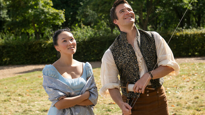 A man and woman in period costumes outdoors, smiling and looking up, promoting TV show release date in February 2026. A man and woman in period costumes outdoors, smiling and looking up, promoting TV show release date in February 2026.