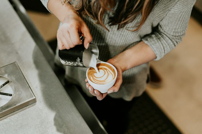 Person pouring milk to create latte art in coffee, showcasing people in boring industries with dramatic behind scenes.