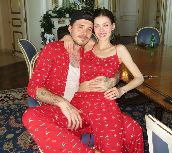 Brooklyn Beckham and woman in matching red outfits seated indoors amid holiday decorations and a dining table.