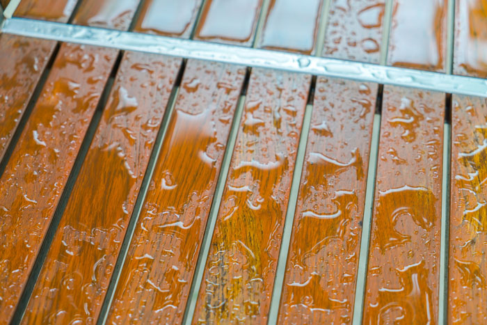 Close-up of a wet wooden surface with water droplets highlighting stains and grime on the slatted wood. Close-up of a wet wooden surface with water droplets highlighting stains and grime on the slatted wood.