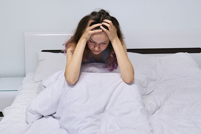 Woman sitting on bed with hands on her head, showing distress and anguish related to stalker tendencies and loss.