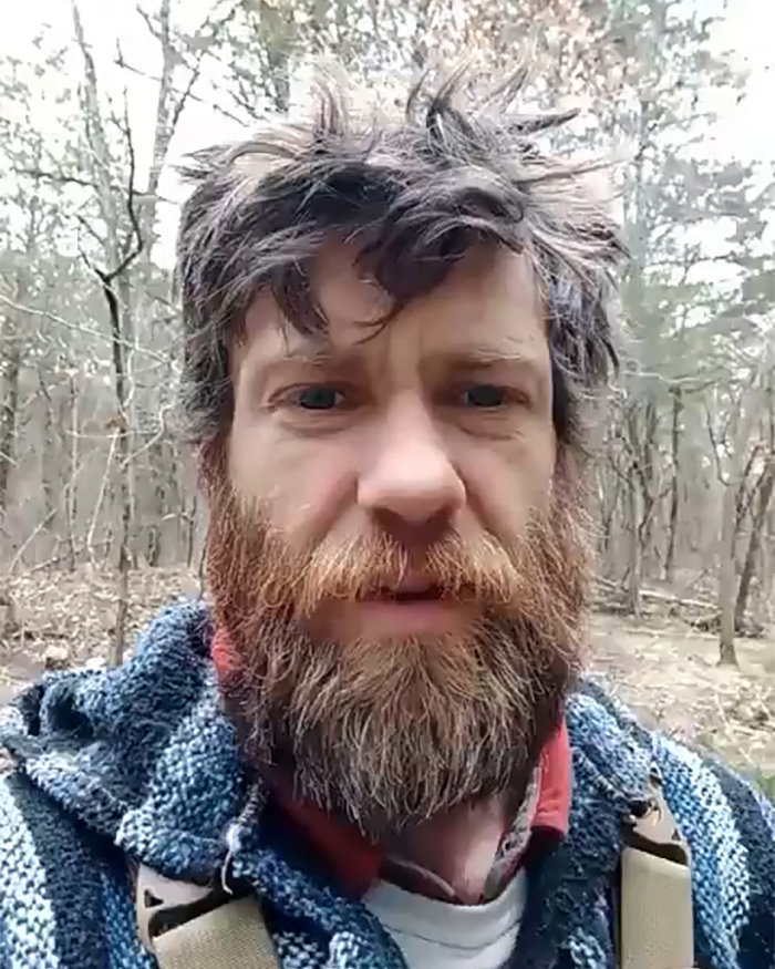 Man with unkempt beard and hair wearing a striped hoodie in a forest, symbolizing poverty and off the grid living. Man with unkempt beard and hair wearing a striped hoodie in a forest, symbolizing poverty and off the grid living.