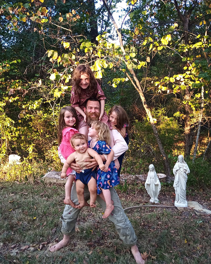 Man living off the grid with children near religious statues in a wooded poverty setting after arrest. Man living off the grid with children near religious statues in a wooded poverty setting after arrest.