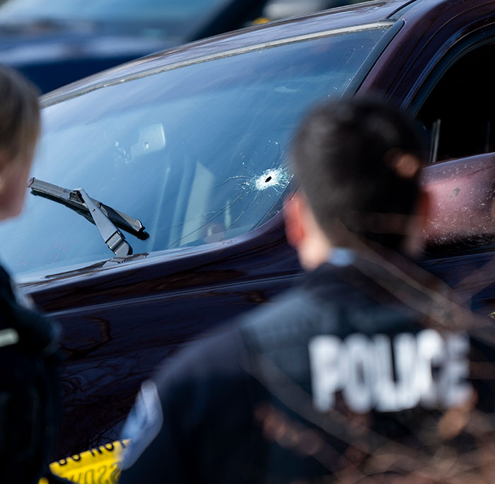 Police officers inspecting a car with a bullet hole in the windshield linked to woman slain by ICE in Minneapolis case.