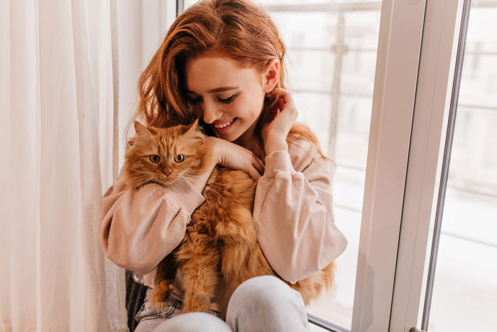 Young woman holding her orange cat indoors, showcasing a loving bond with a lost cat turned family royalty.