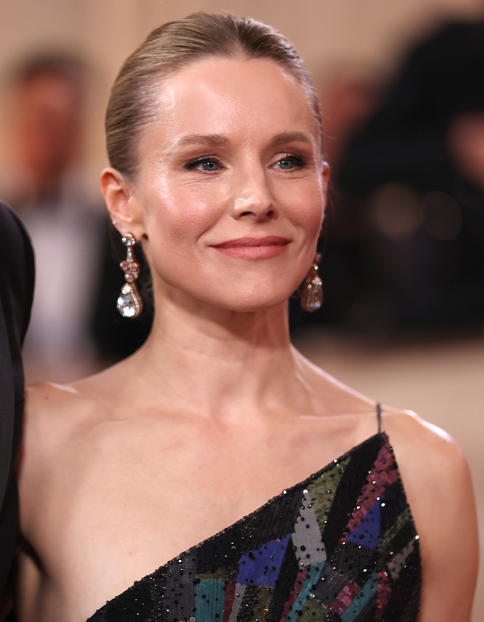 Woman with glowing skin at an event, wearing statement earrings and a colorful sequin dress, showcasing celeb facialist glow.