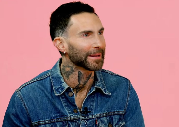 Man with neck tattoos and beard wearing a denim jacket against pink background in a celebrity infidelity scandals feature.