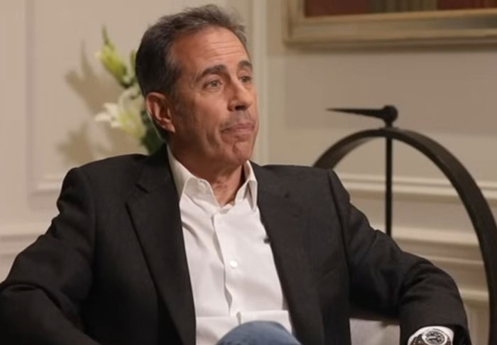 Man in a dark blazer and white shirt in an interview setting discussing celebrity infidelity scandals and controversies.