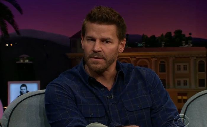 Man in a blue checkered shirt speaking on a late-night talk show about celebrity infidelity scandals.