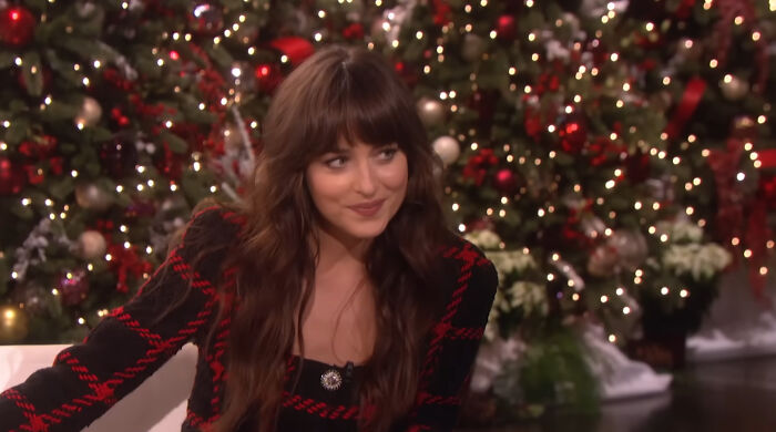 Actress with long brown hair smiling during an interview, with a festive holiday background and Christmas decorations.
