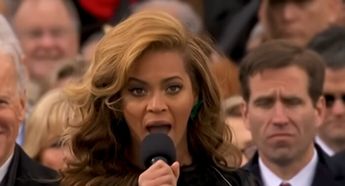 Beyoncé delivering a powerful speech into a microphone with a serious crowd behind her, showing savage responses.