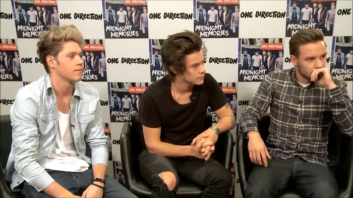 Three members of One Direction sitting in an interview setting reacting with annoyed and thoughtful expressions.