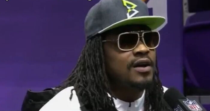 A celebrity wearing sunglasses and a cap giving a savage response during an interview with a microphone.