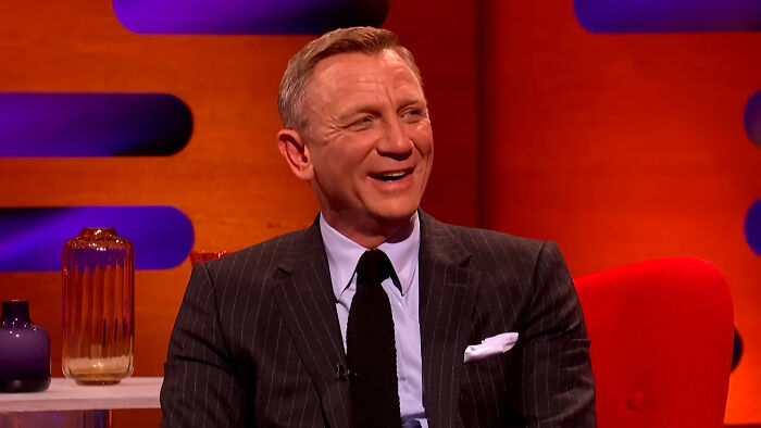 Actor Daniel Craig in a dark pinstripe suit smiling during a TV interview with savage responses to annoying questions.