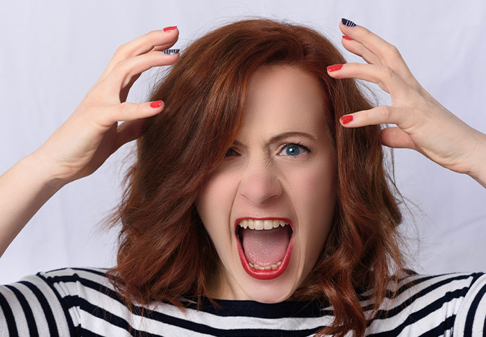 Frustrated woman with red hair and striped shirt expressing shock, illustrating celebrity out of touch with reality moments.