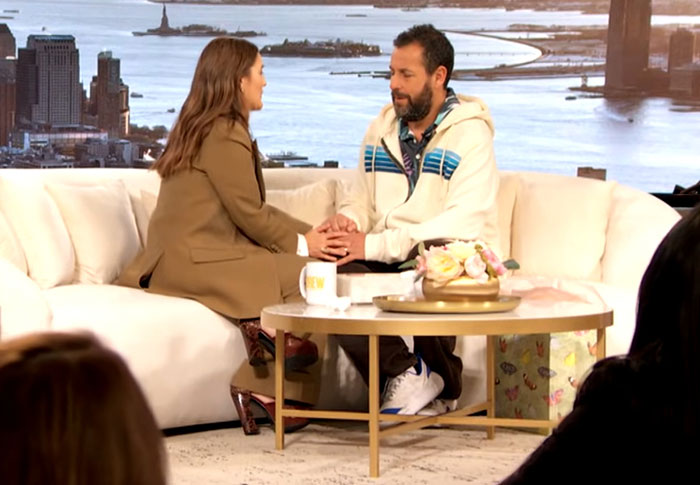 Celebrity couple holding hands on a talk show set, showing moments when celebrities were out of touch with reality.