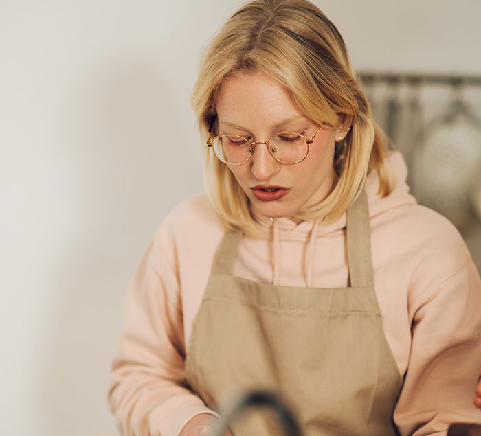 Blonde female chef wearing glasses and an apron, focusing on cooking indoors, avoiding restaurants with boyfriend or girlfriend