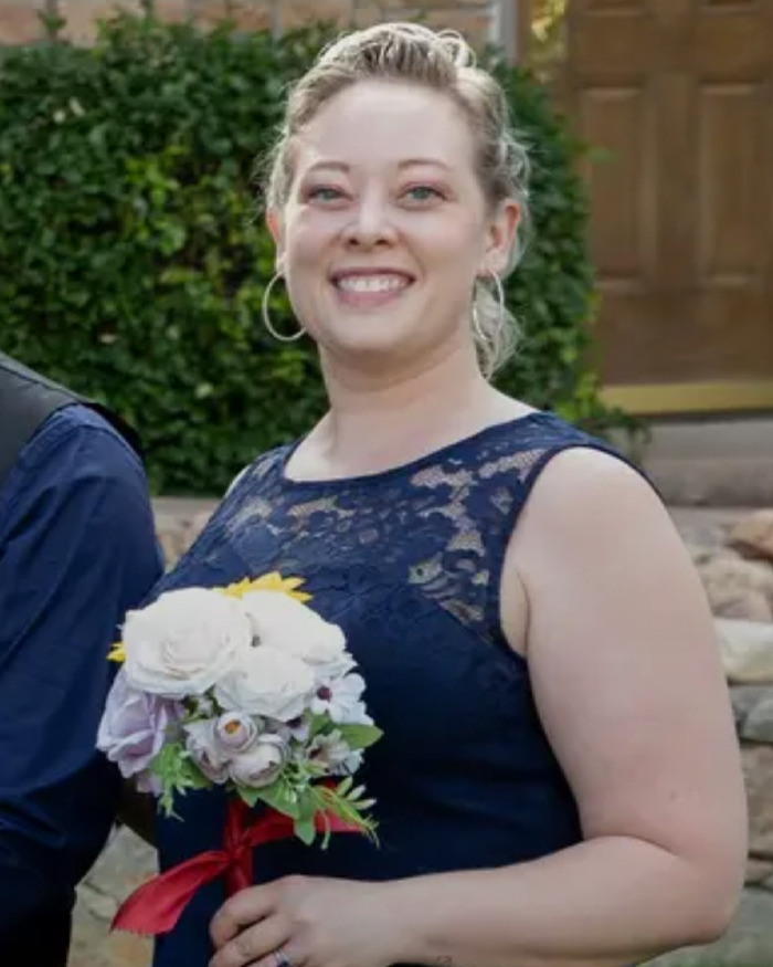 Smiling woman in navy lace dress holding a bouquet of flowers, related to ICE video and fatal shooting context.