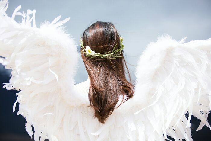 Woman in angel wings and flower crown seen from back, symbolic image for hospital workers and patients' last words