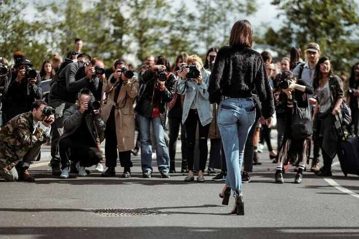 Photographers taking pictures of a woman walking confidently, illustrating adult goals that seem overrated in modern life.