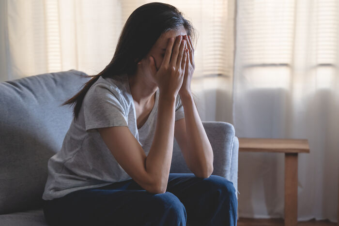 Woman sitting on couch covering her face, distressed after boyfriend mocks her gift and demands space following work trip.
