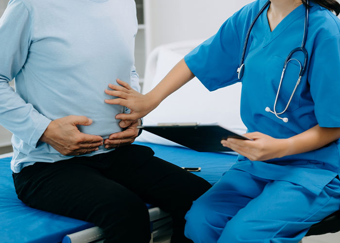Nurse in blue scrubs examining patient's abdomen, showing health signs of abdominal pain and discomfort