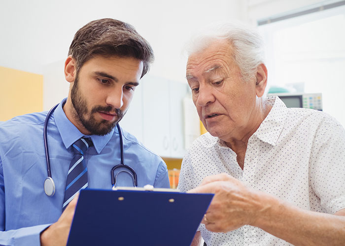 Doctor reviewing clipboard with elderly patient, discussing health signs and concerns in clinic.