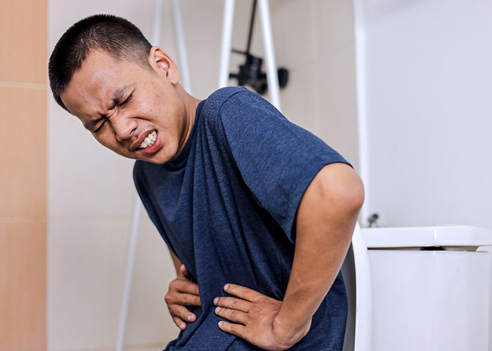 Man clutching abdomen while sitting on toilet, grimacing in pain, illustrating health signs of serious issues
