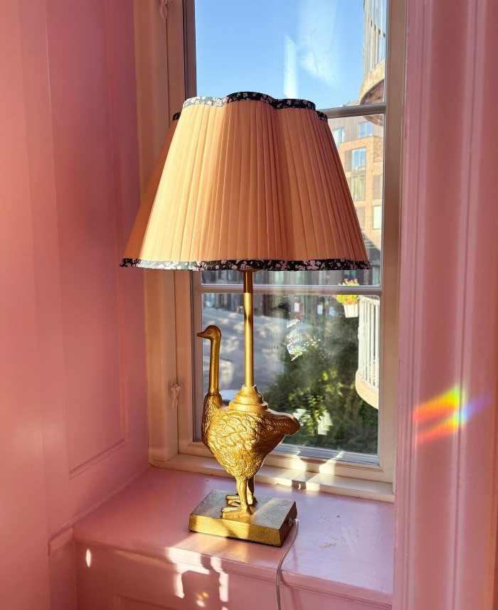 Gold bird-shaped lamp with pleated shade on a pink windowsill showcasing cool interior design ideas.