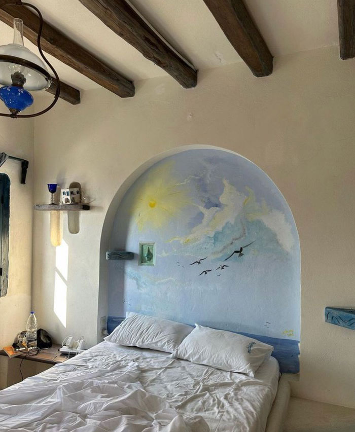 Cozy bedroom interior design ideas with painted sky mural, wooden beams, and natural light creating a relaxing atmosphere.