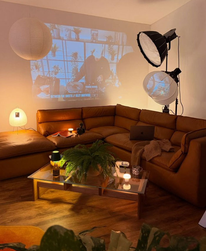 Cozy living room with warm lighting, leather sectional, modern glass coffee table, and trendy interior design ideas.