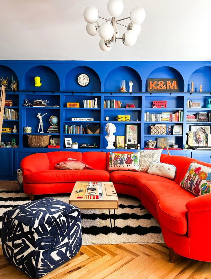 Vibrant living room with bright red curved sofa, patterned pillows, bold blue built-in shelves, and modern interior design ideas.