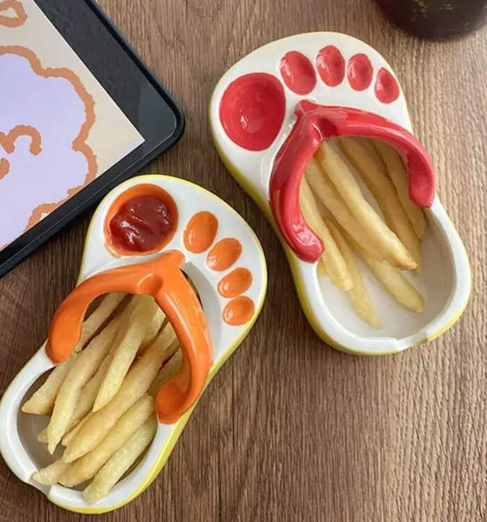 Two foot-shaped ceramic dishes with ketchup and french fries on a wooden table, creative interior design ideas.