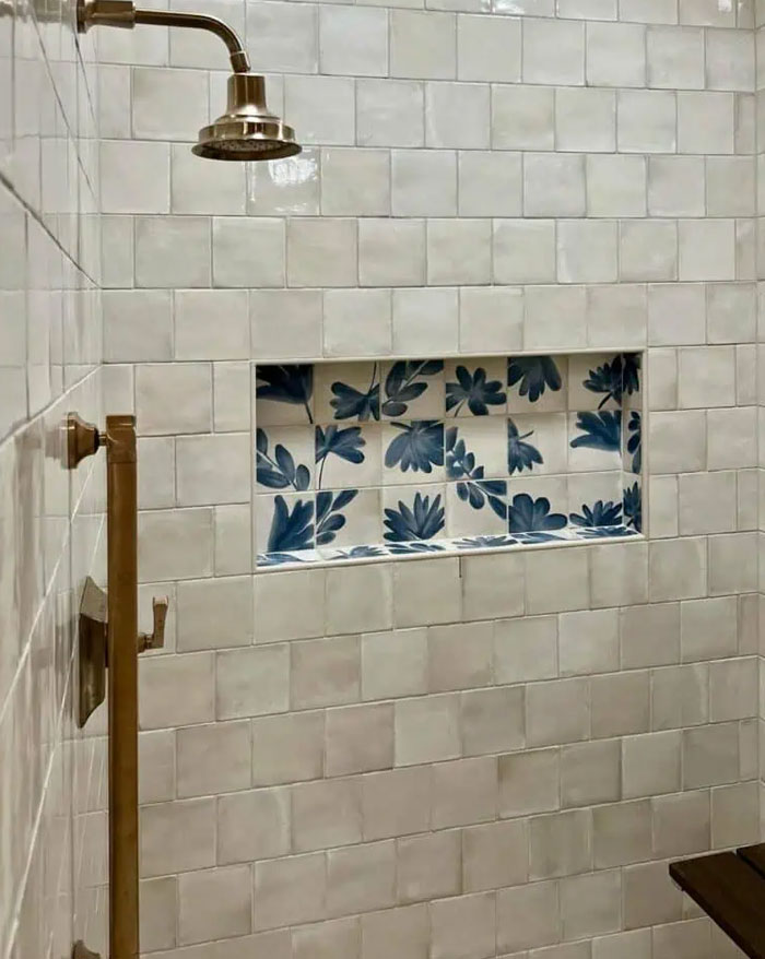 Bathroom shower interior design with white square tiles and a recessed niche featuring blue floral tiles for decoration.