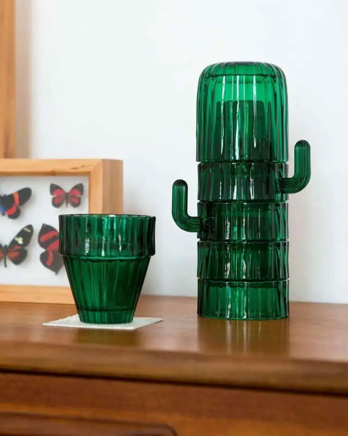 Green glass cactus-shaped stackable cups and a matching tumbler on wooden furniture in a modern interior design setting.
