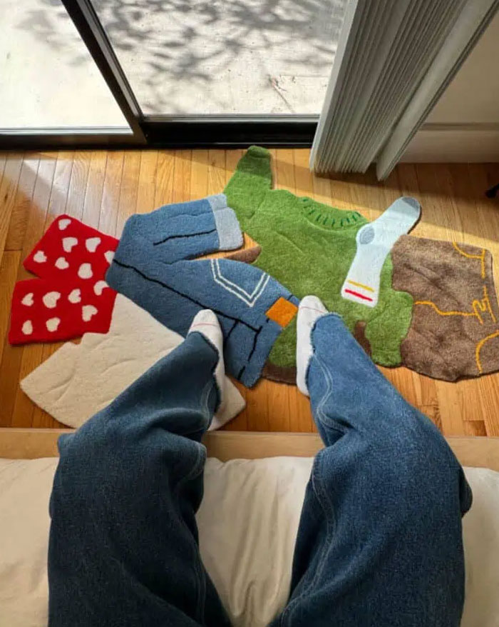 Person wearing jeans sitting indoors near colorful rugs shaped like clothing items, showcasing cool interior design ideas.
