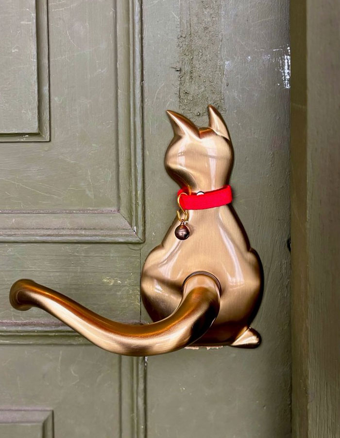 Manija de puerta con diseño de gato en metal dorado y collar rojo como idea de diseño interior original y cool.