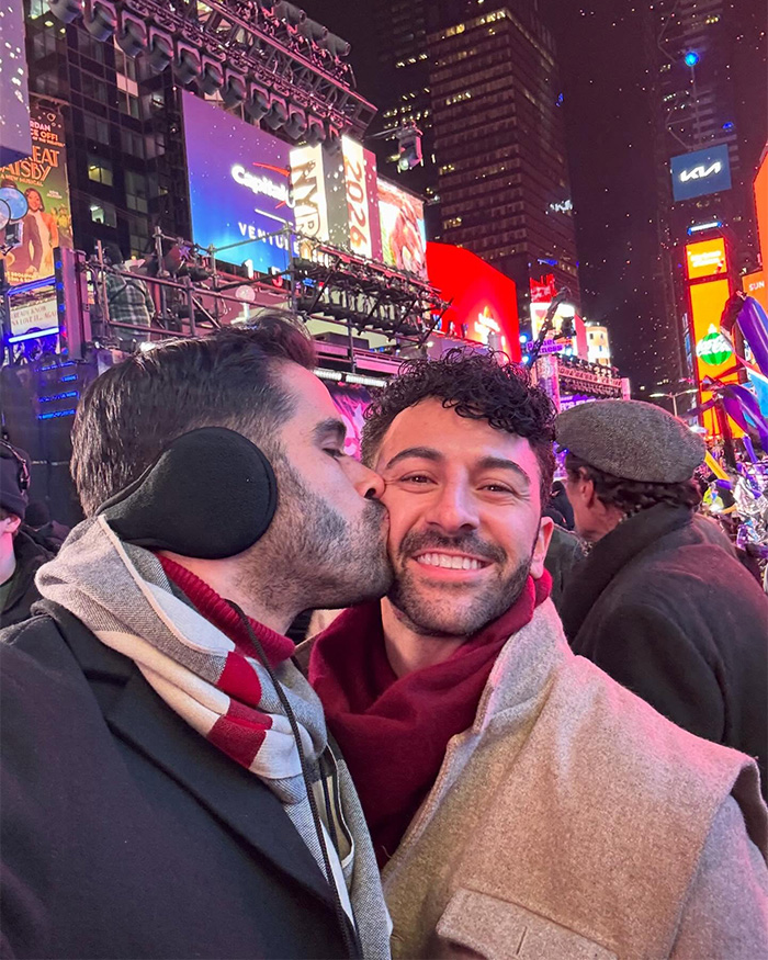 Gay couple in Times Square on New Year's Eve, one man kissing partner's cheek amid bright billboards and crowd Gay couple in Times Square on New Year's Eve, one man kissing partner's cheek amid bright billboards and crowd