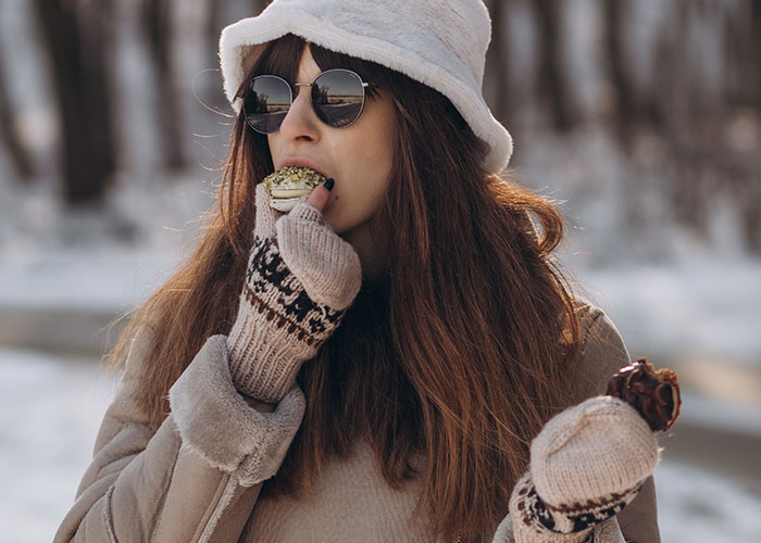 Woman wearing winter clothes and sunglasses outdoors, enjoying snacks while reflecting on couples' dumb house rules.