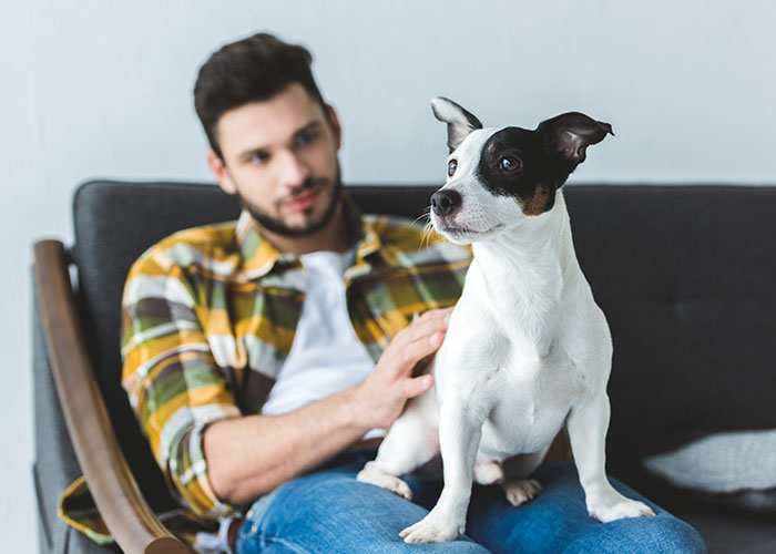 Man in a plaid shirt sitting on a couch with his dog, illustrating couples sharing dumb house rules seriously.