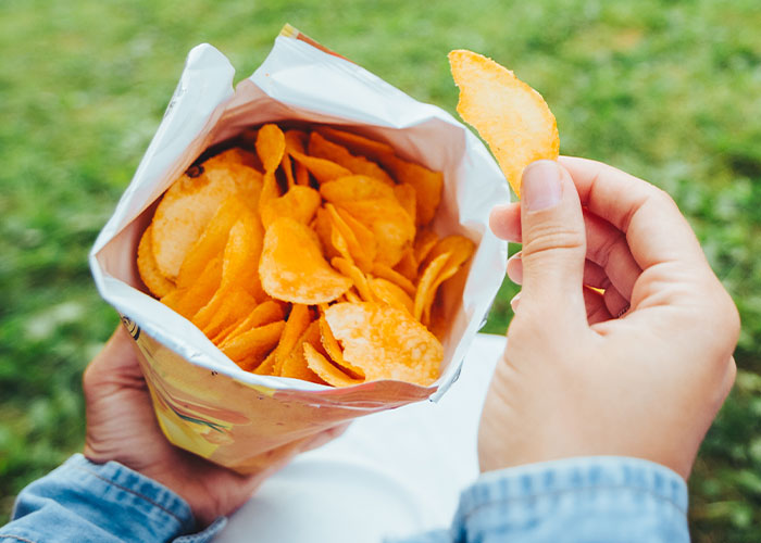 Hands holding a bag of potato chips outdoors, illustrating couples sharing dumb house rules as a joke now taken seriously.